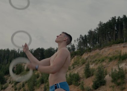 Young guy in speedos juggles on a wild beach